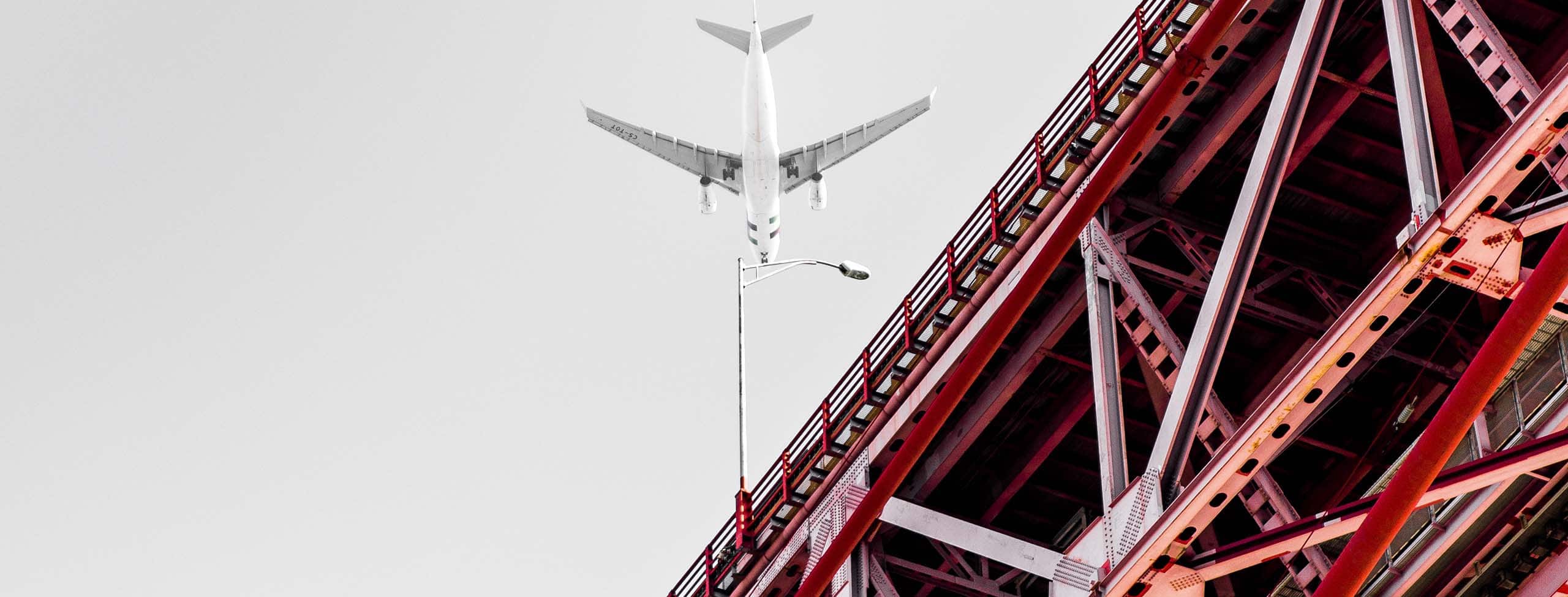 airplane flying over a red bridge