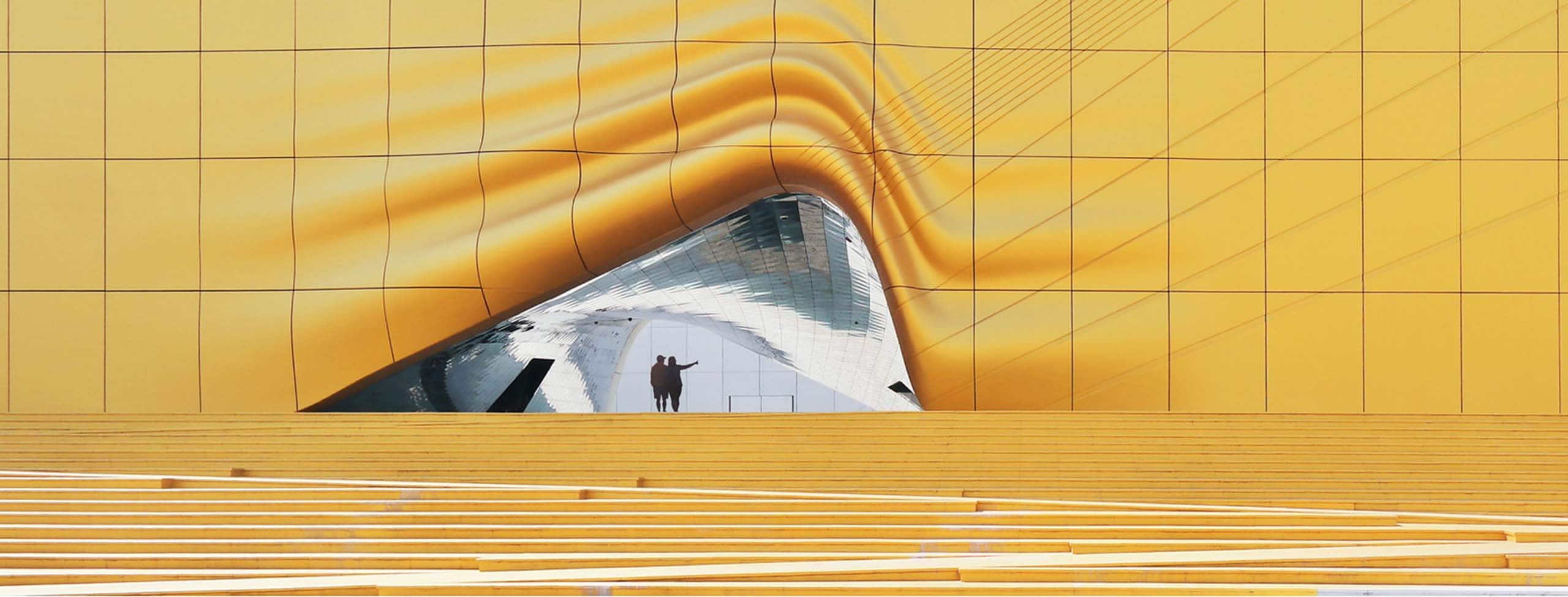 Abstract gold exterior of a building with people walking through an entrance in it  